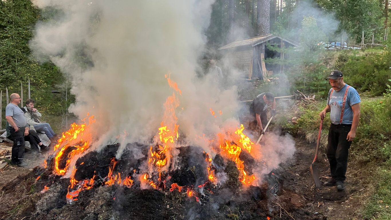 Muutama ihminen palavan tervahaudan äärellä, takan