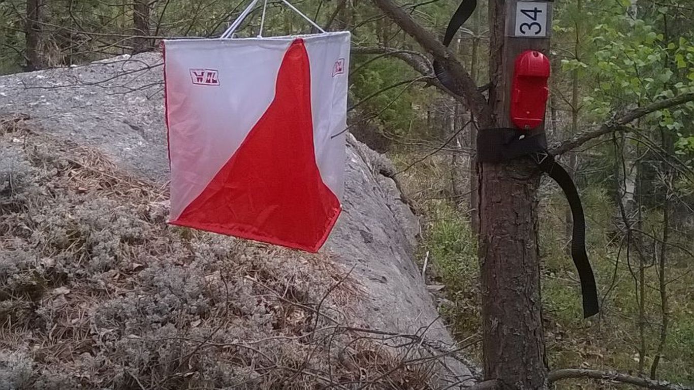 Kuvassa on rastilippu ja leimauslaite, jossa emit-